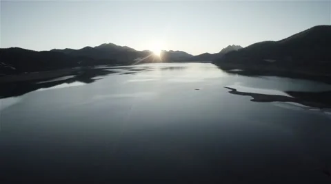 Drone view of a lake with sunset and sun appearing behind the mountains. Video stock 51386583