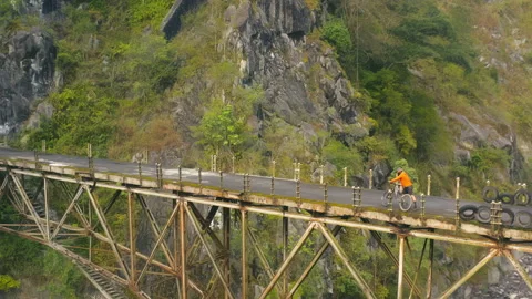 Drone view of man on bicycle riding on suspension bridge in mountains Stock Footage 130670406