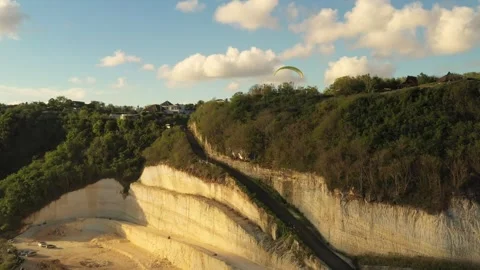 Drone view of a man flying on a yellow paraglider over a hill and trees towards  Stock Footage 254425857