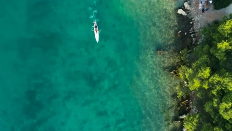 Drone view of a man laying on a surf board on a calm sea by the coast Stock Footage 132764058