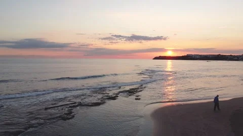 Drone view of man walking against sunset by the sea Stock Footage 227440961
