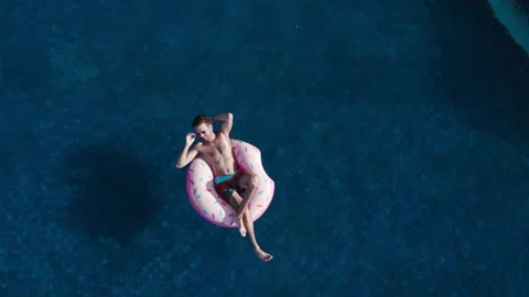 Drone view of millennial man sunbath, swim with inflatable mattress donut Stock Footage 269890393
