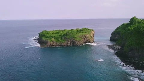 Drone view over the ocean with islet and cliffside covered with lush greenery. Stock Footage 137444943
