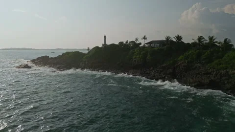 Drone view over ocean shows waves hitting rocky coast with hilltop lighthouse Stock Footage 270328918