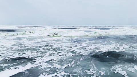 Drone view over textured sea ice with dark thin-ice patches and a distant Stock Footage 333033167