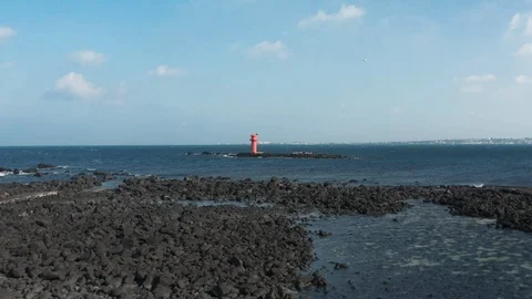 Drone view over the volcanic basalt to the red lighthouse and horizon. Jeju. Stock Footage 122272510