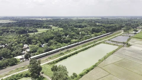 Drone view of passenger train crossing green rural farmland and ponds area Stock Footage 344544146