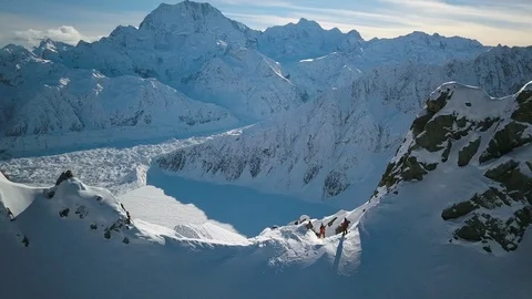 Drone view of pro athletes standing on snowy mountain ridge with sky background Stock Footage 121580337