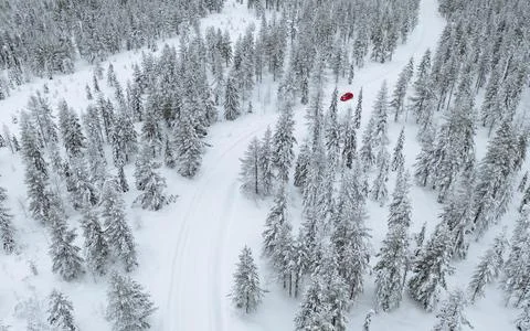 Drone view of a red car driving though a snowy forest in Lapland, Finland Stock Photos