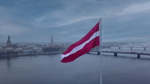 Drone View Of Riga Old Town With Latvian Flag Waving In Foreground Aerial Pan Стоковые фото