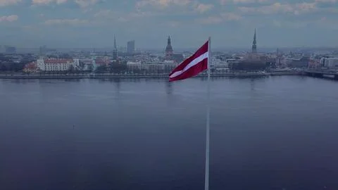 Drone View Of Riga Old Town With Latvian Flag Waving In Foreground Aerial Pan 库存照片