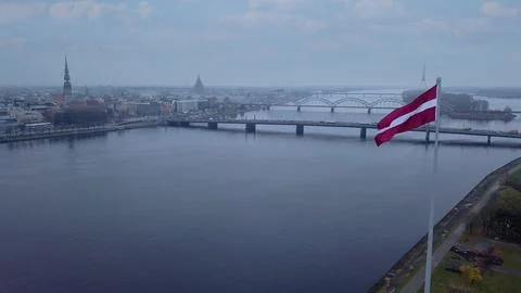 Drone View Of Riga Old Town With Latvian Flag Waving In Foreground Aerial Pan 库存照片