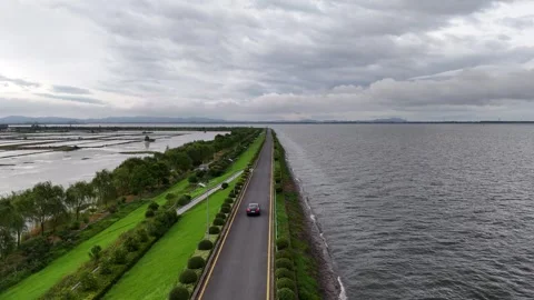 Drone view of road beside lake and wetlands under cloudy sky in China Stock Footage 337767989