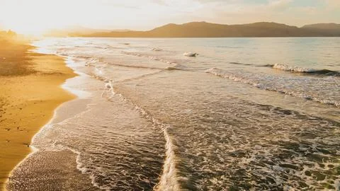 Drone view of sandy beach with gentle waves lapping on shore under warm gol.. Foto stock