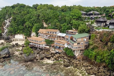 Drone view shows cliffside beachfront resort with thatched roofs above rock.. Fotos Stock