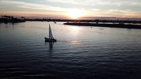 Drone view of small sailboat at sunset with SUP, kayakers, palms, and seagulls Stock Footage 84775294