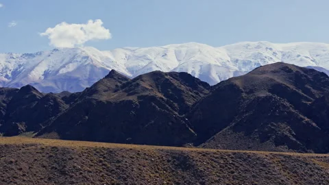 Drone view of snow-capped mountains under a blue sky with single cloud in Stock Footage 328732072