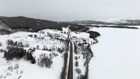 Drone view of a snowy landscape in Norway, showcasing a curved asphalt road Stock Footage 330376542