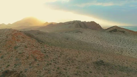 Drone view Sunbeams over rugged coastal mountains, turquoise sea at golden hour Video stock 337956000