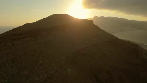 Drone view Sunbeams over rugged coastal mountains, turquoise sea at golden hour Video stock 337957551