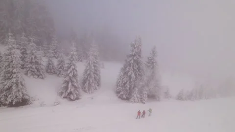 Drone view of three hikers crossing snowy mountain slope in dense fog near Stock Footage 346542145