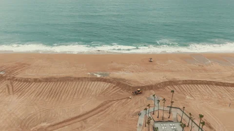 Drone view of a tractor moving across sandy Newport Beach near ocean waves Stock Footage 347744749