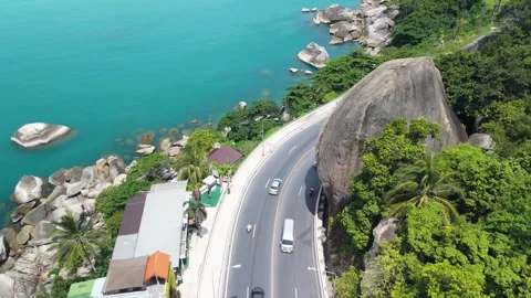 Drone view. Turquoise ocean water washes against rocky coastline as cars and Stock Footage 312748892