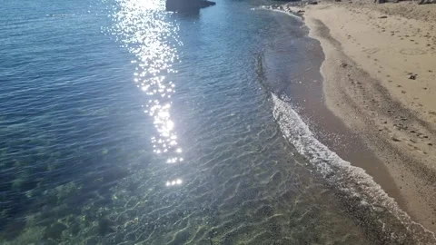 Drone view of waves washing sandy shoreline under bright shimmering sunlight Video stock 322161146