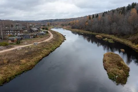 Drone view of a wide dark river with a grassy island curving past a traditional Stock Photos