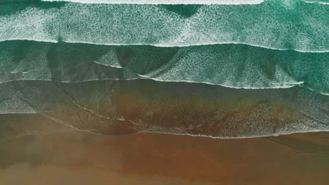 Drone view of wide turquoise sea waves rolling onto dark sandy coast in slow Stock Footage 345693804