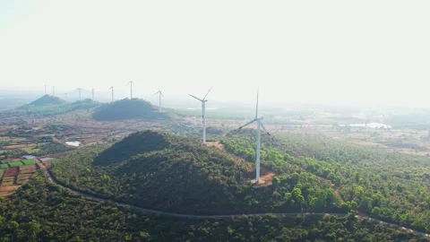 A drone view of wind turbines stand against misty sky surrounded by lush gr.. Vídeo Stock 346701202