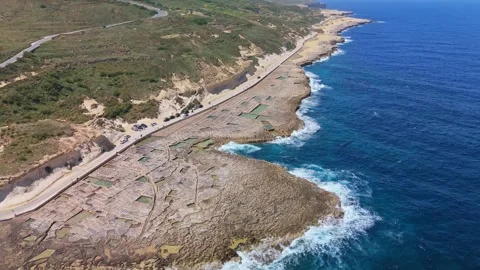 Drone view of Xwejni salt pans in Żebbuġ Gozo as people walk along the coast Stock Footage 335836656
