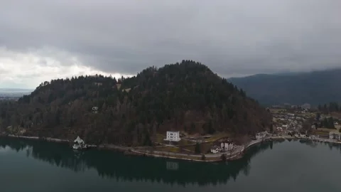 A drone views Lake Bled's calm waters reflecting an overcast sky and forests Stock Footage 336467699