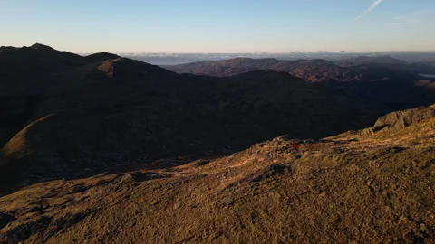 Drone wide pull back and pan of woman on ridge with distant Isle of Skye horizon Stock Footage 327915278