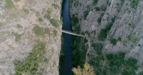 Drone zenith descent to deep ravine and to the bottom suspension bridge Stock Footage 124389325