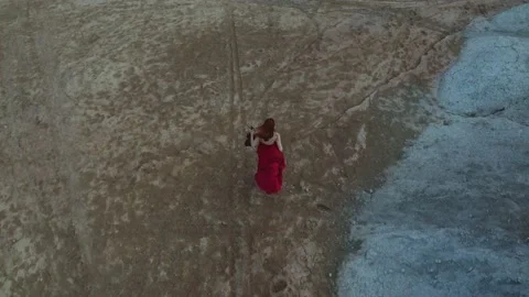 Drone's camera is flying by girl in a red dress with long red hair running with  Video stock 229410393