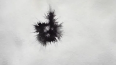 A drop of black paint falls on the white surface and spreads over it Stock Footage 147502603