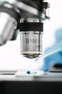 Drop of blue liquid on slide at microscope to make coronavirus test in lab Stock Photos