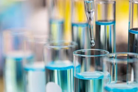 Drop of clear blue liquid from droper droping to test tube in laboratory with Stock Photos