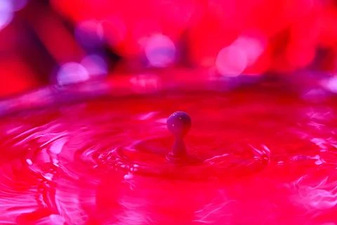 A drop falls into a dense liquid with a red background. Abstract colorful Stock Photos