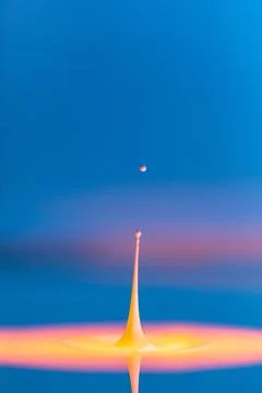 A drop falls into a thick liquid with a blue-yellow background. Abstract co.. Stock Photos