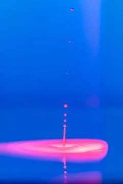 A drop falls into a thick liquid with a blue-pink background. Abstract colorful Stock Photos