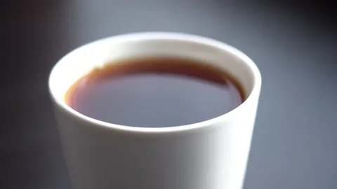 A Drop Falls into a White Mug with Black Tea on a Black Table in Daylight Stock Footage 167885546