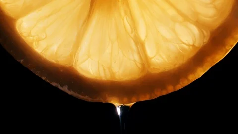 A drop of juice flows down from a slice of lemon on a black background in macro Stock Footage 127855043