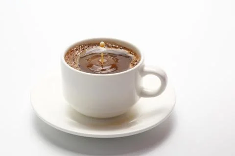 Drop of milk falling in a white cup with black coffee Stock Photos