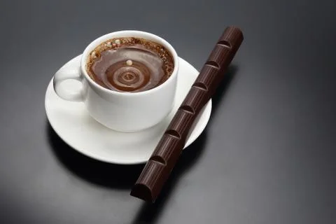 Drop of milk falling in a white cup with black coffee Stock Photos