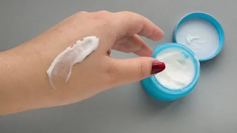 A drop of moisturizer on the hand close-up, a jar of cream on the table. Anti Stock Footage 324554137