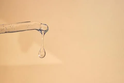 A drop of moisturizing liquid for facial skin drips from a pipette on a beige Stock Photos