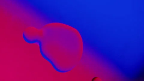 A drop of oil connects with another drop on a blue-red gradient background. 스톡 동영상 303058567