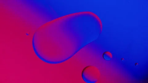A drop of oil connects with another drop on a blue and red gradient background. Stockbeeldmateriaal 303058784